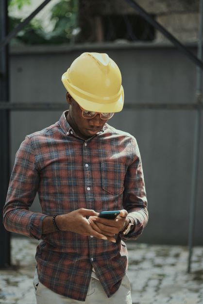 Man in hard hat looking at mobile cell phone on construction site